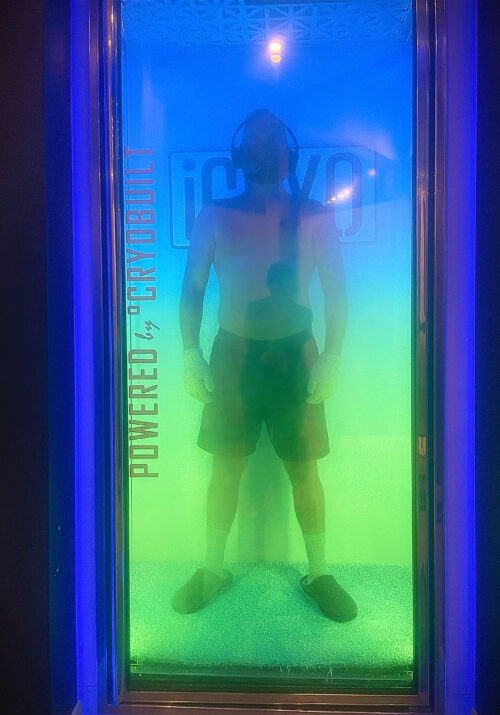 Man standing in a cryotherapy chamber with mist rising around him, undergoing cold therapy for health and recovery.